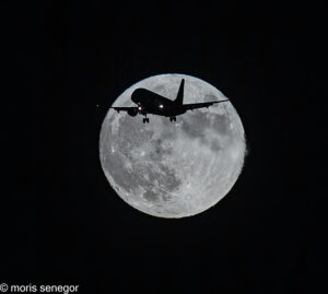 B&W image of a plane flying by a large full moon